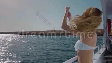 慢动作。 自由的概念。 穿比基尼的金发美女，坐在游艇上。 她解开头发。 头发